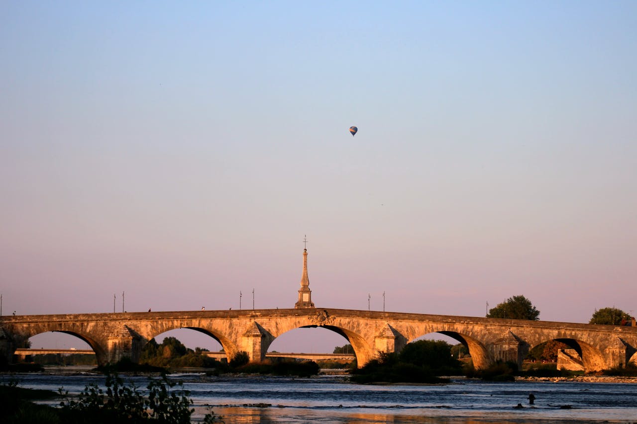 A picturesque view of a historic stone bridge at sunset with a hot air balloon in the sky.