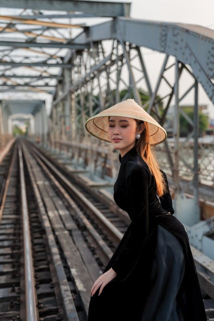 Woman in traditional straw hat posing on a metal railway bridge, capturing a blend of culture and architecture.